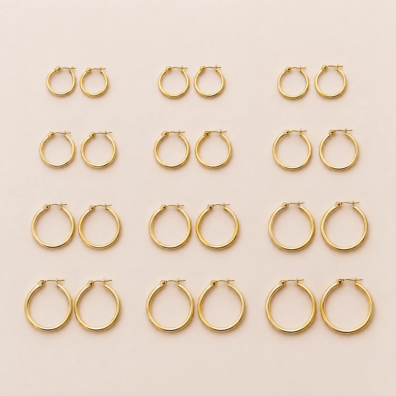 Twelve pairs of plain gold-tone hoop earrings in graduated sizes on a blush background