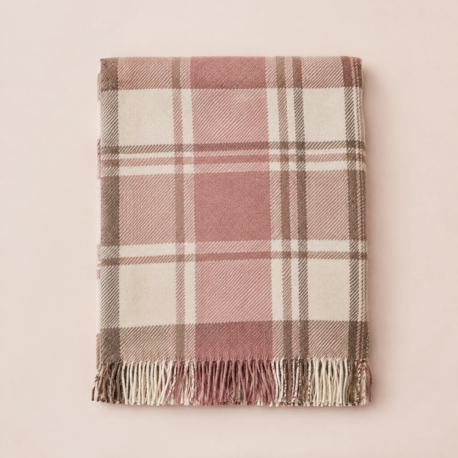 Folded cream and rose plaid blanket scarf with fringed ends on a blush background