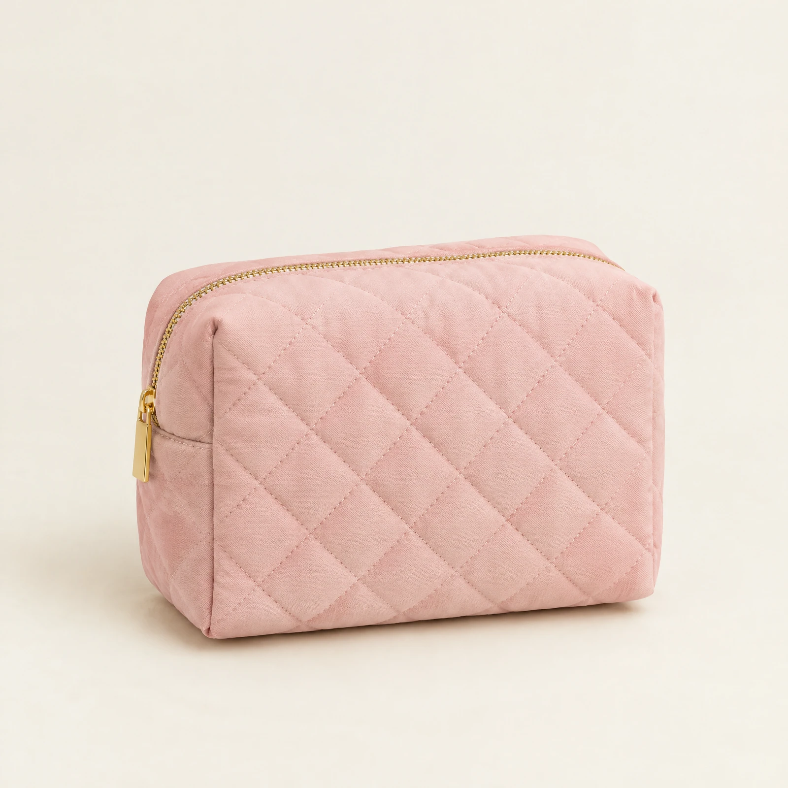 Blush pink quilted zip pouch with a gold-tone zipper on a cream background