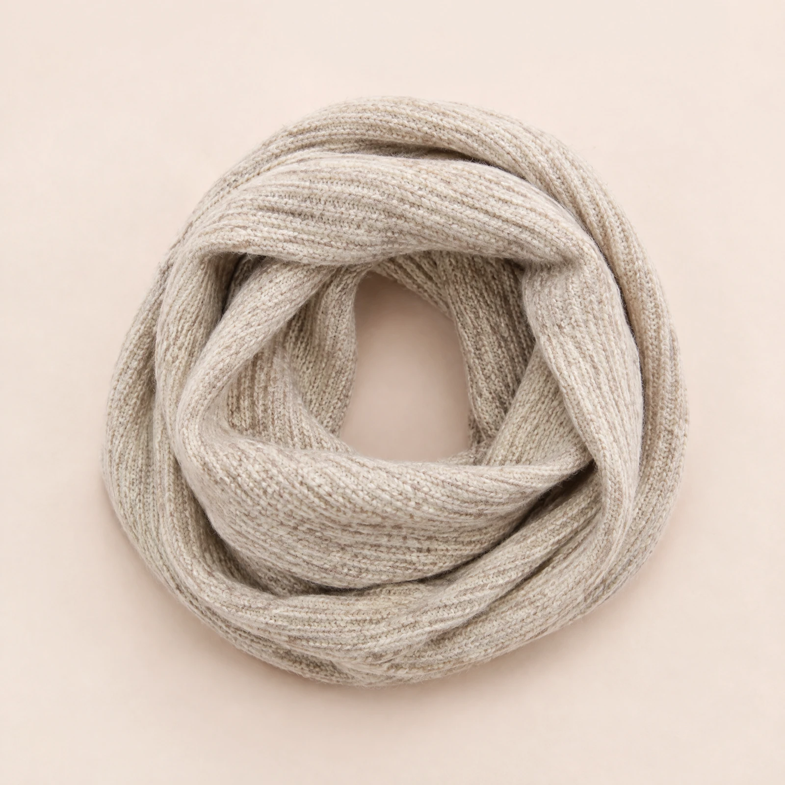 Oatmeal ribbed infinity scarf laid in soft loops on a blush background
