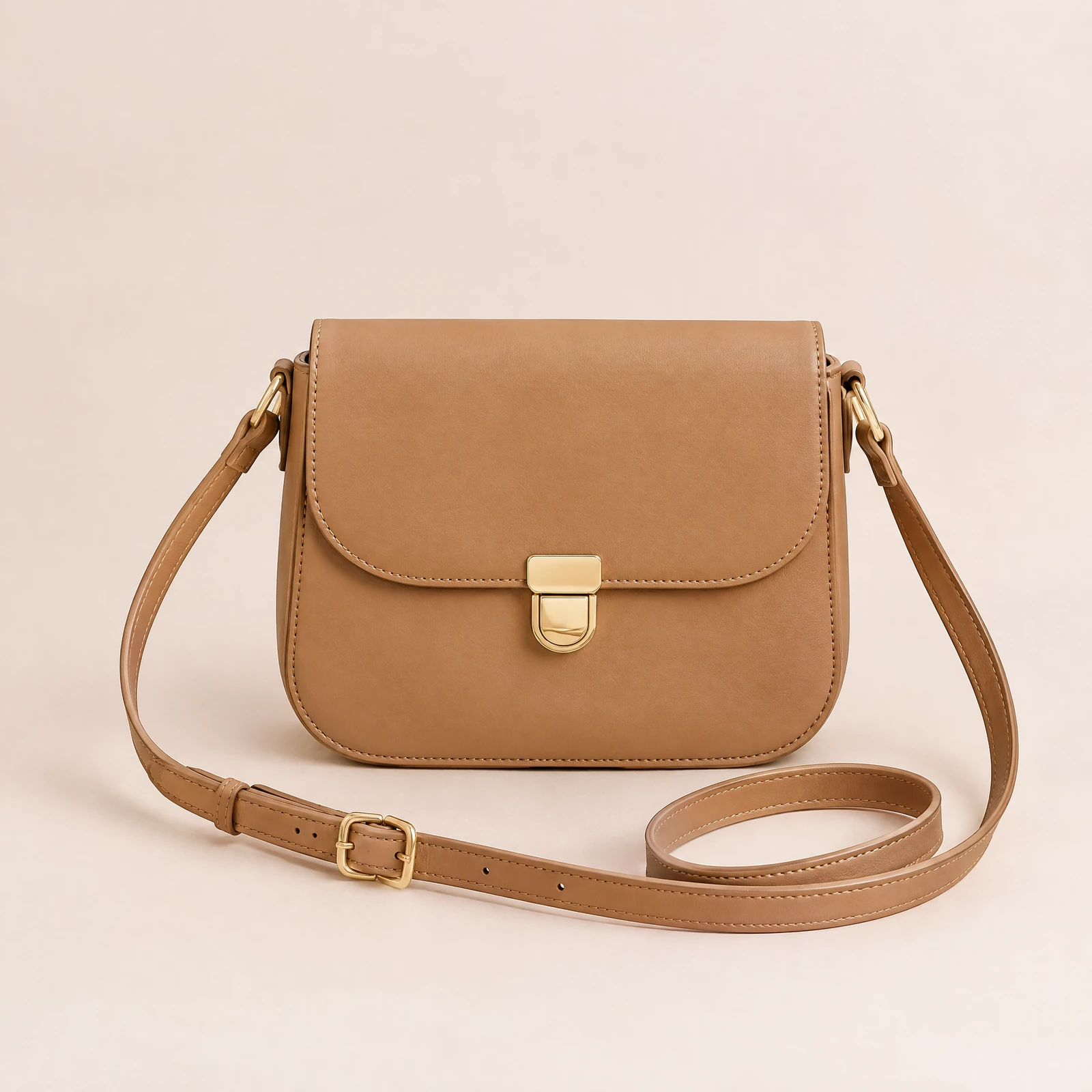 Tan crossbody bag with front flap and gold-tone clasp on a blush background